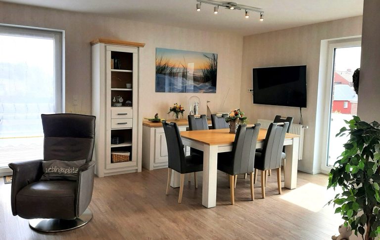 Moderne Wohnküche mit Holztisch, Stühlen, TV und großen Fenstern.