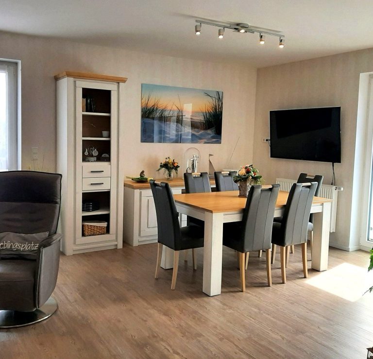Heller Wohn- und Essbereich der Ferienwohnung Tillmanns Stadtlounge in Norden mit großem Esstisch, Fernseher und gemütlichem Sessel.