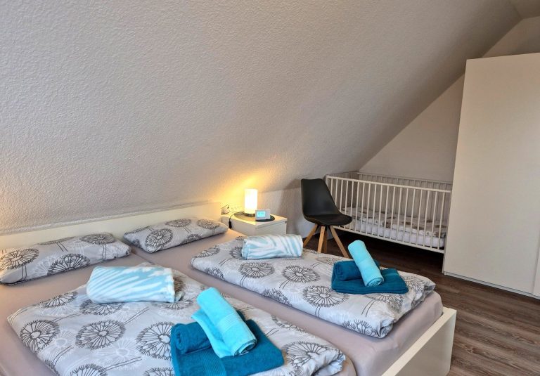 Gemütliches Schlafzimmer der Ferienwohnung Tillmanns Pusteblume in Norddeich mit Doppelbett, Babybett und maritimen Farbakzenten.